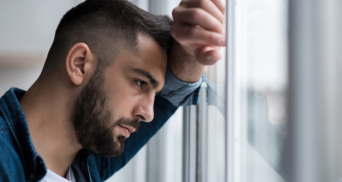 Man looking sad while resting his head on his hand on a window